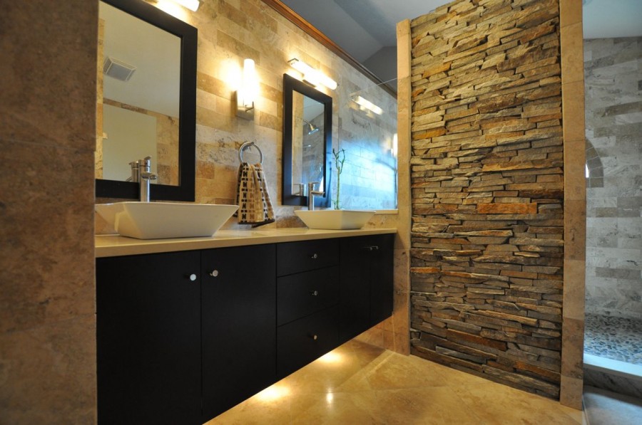 Bir duvarı doğal taş ile süslenmiş banyo, modern lavabolar ve aplik aydınlatmalar